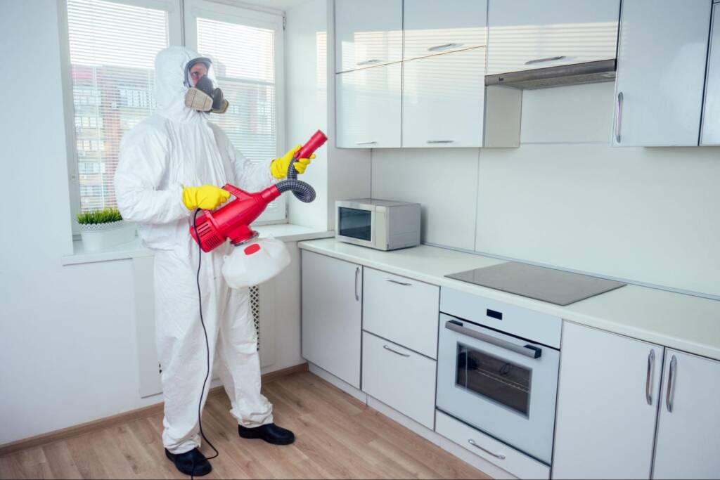 A pest control worker in a protective suit and gear, ready to spray pesticide in the kitchen.